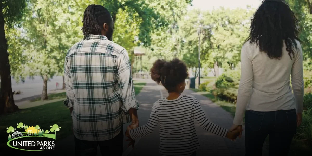 A family walks hand-in-hand down a tree-lined park path on a sunny day, symbolizing connection, safety, and community in Newark’s green spaces.