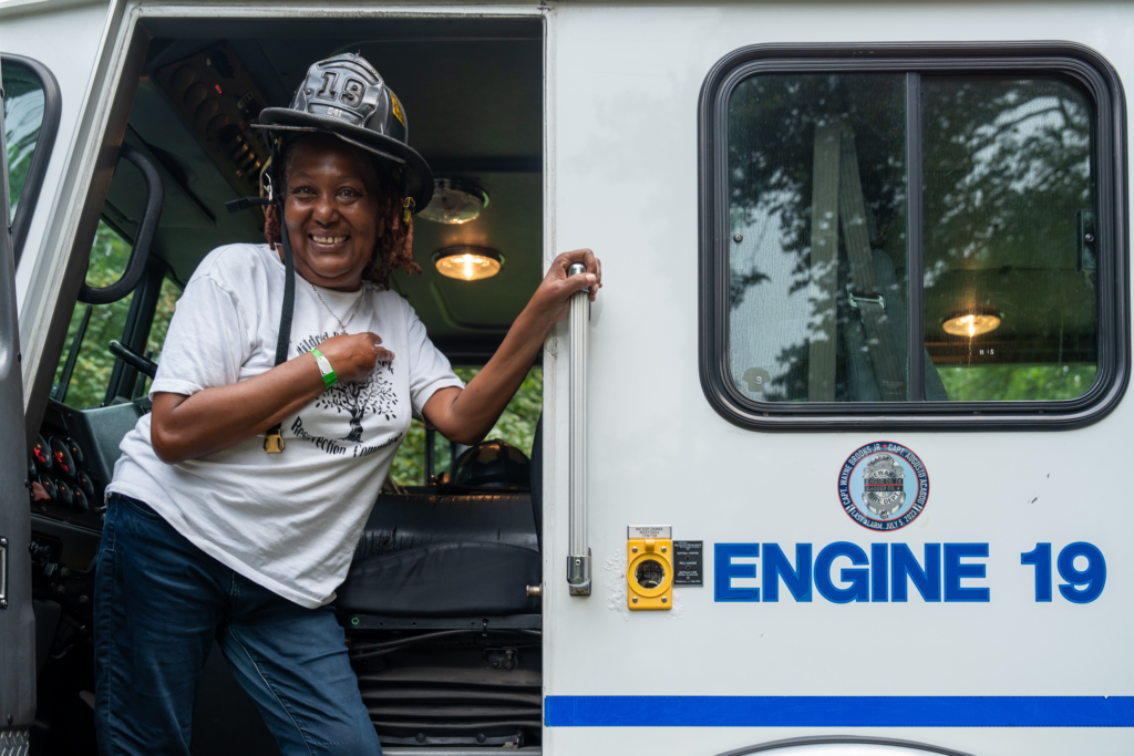 Firefighter smiling while standing in a fire truck at Mildred Helms Park community event