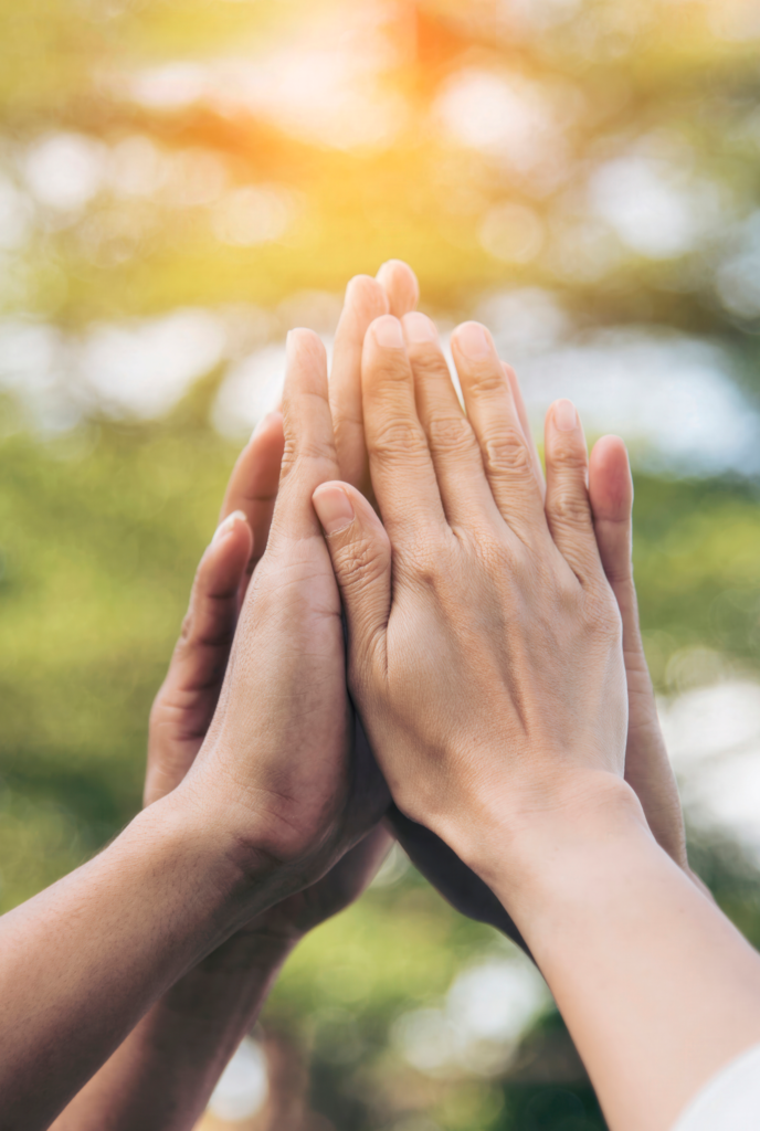 Two hands pressed together in a gesture of partnership and collaboration, with a soft outdoor background.